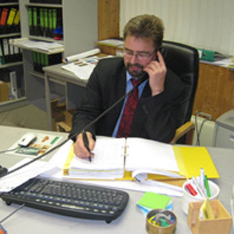 Ein Mann im Anzug führt ein Telefonat und notiert etwas im Büro.